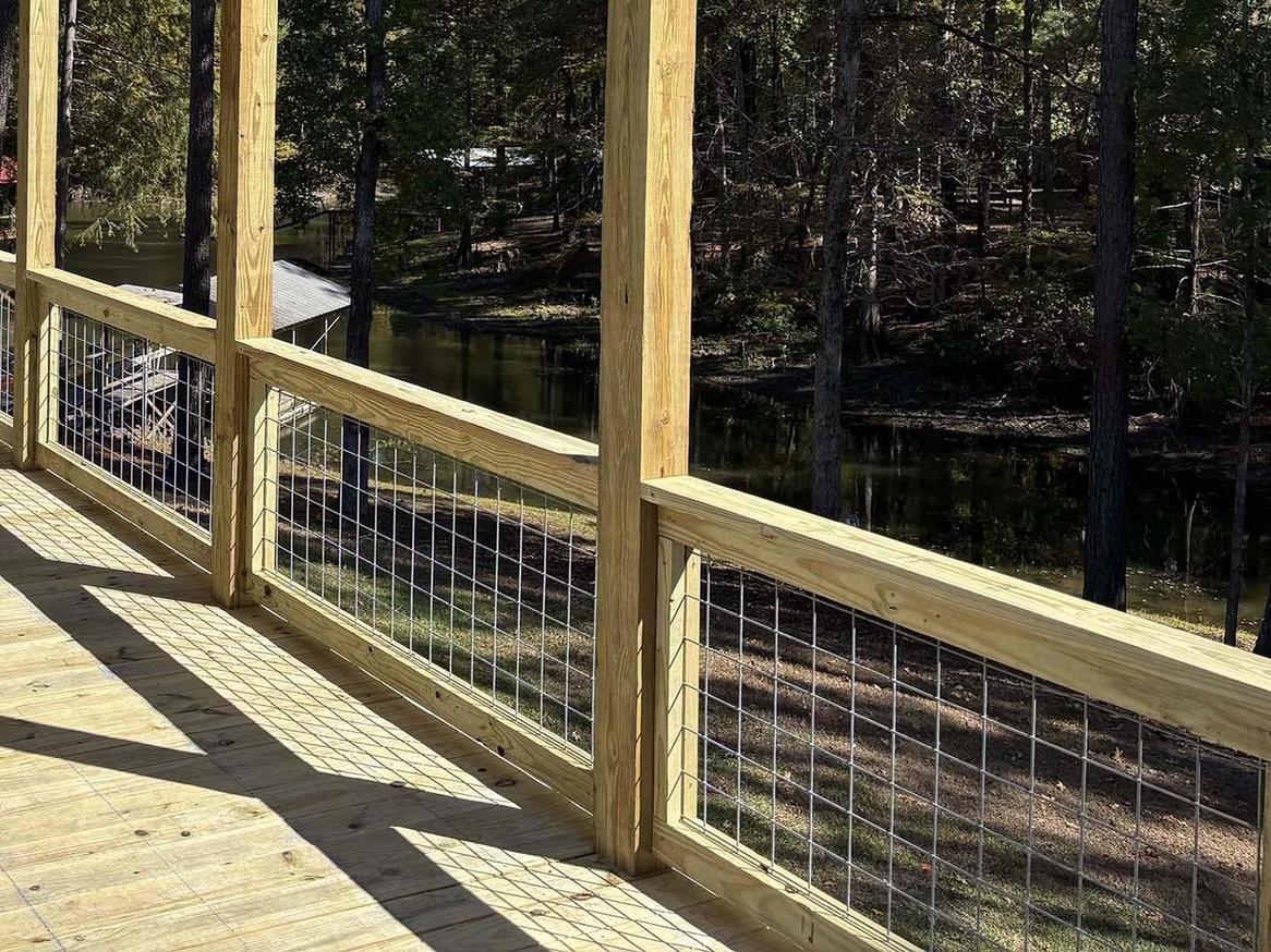 Wood deck railing with wire mesh panels overlooking a wooded lakefront