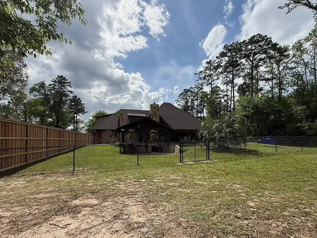 Black vinyl-coated chain link fence enclosing a wooded backyard