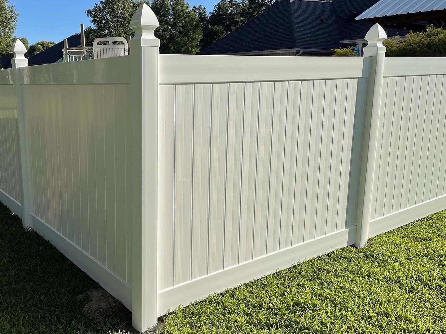 Cream vinyl privacy fence with french gothic post caps beside a manicured lawn