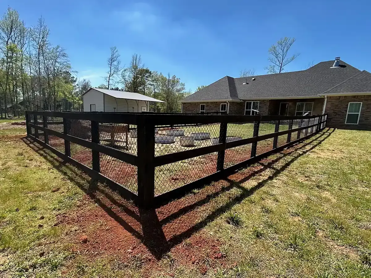 Black wood post and rail ranch fence with chain link mesh infill around a residential yard