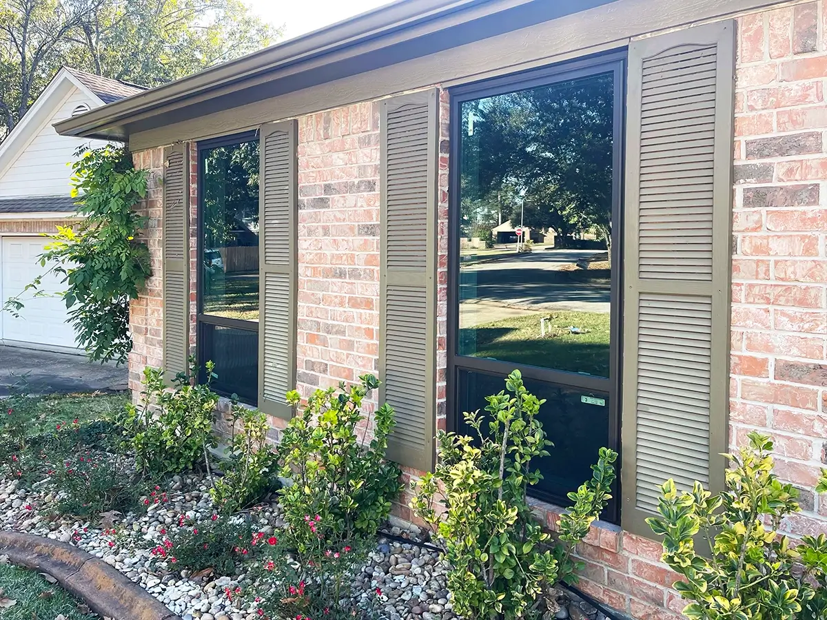Aluminum windows with wood shutters installed on the side of a brick home